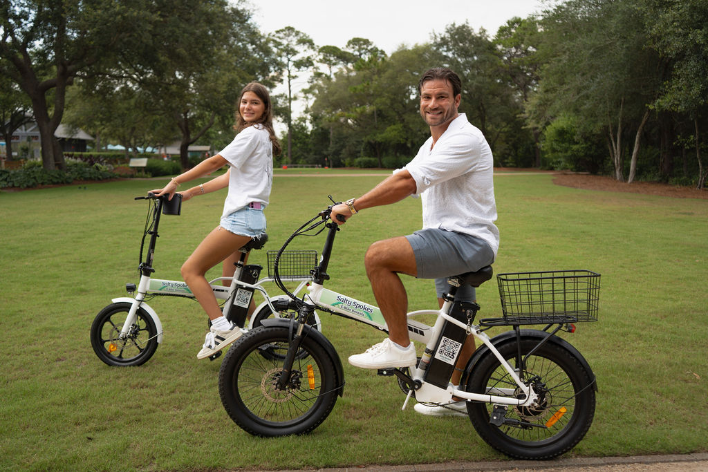 Two riders pausing on Salty Spokes e-bikes on a grassy lawn