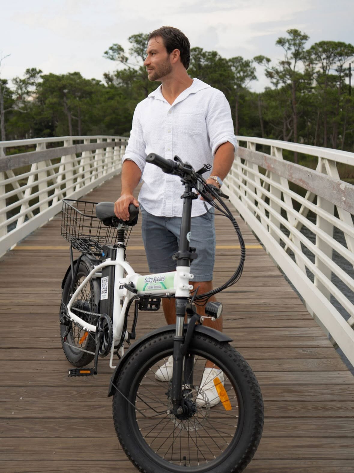 Rider standing with a Salty Spokes e-bike on a wooden bridge